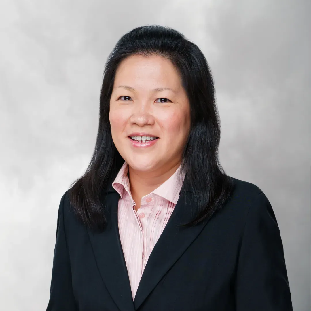 Professional headshot of a woman with shoulder-length black hair wearing a black blazer and a light pink collared shirt against a neutral background.